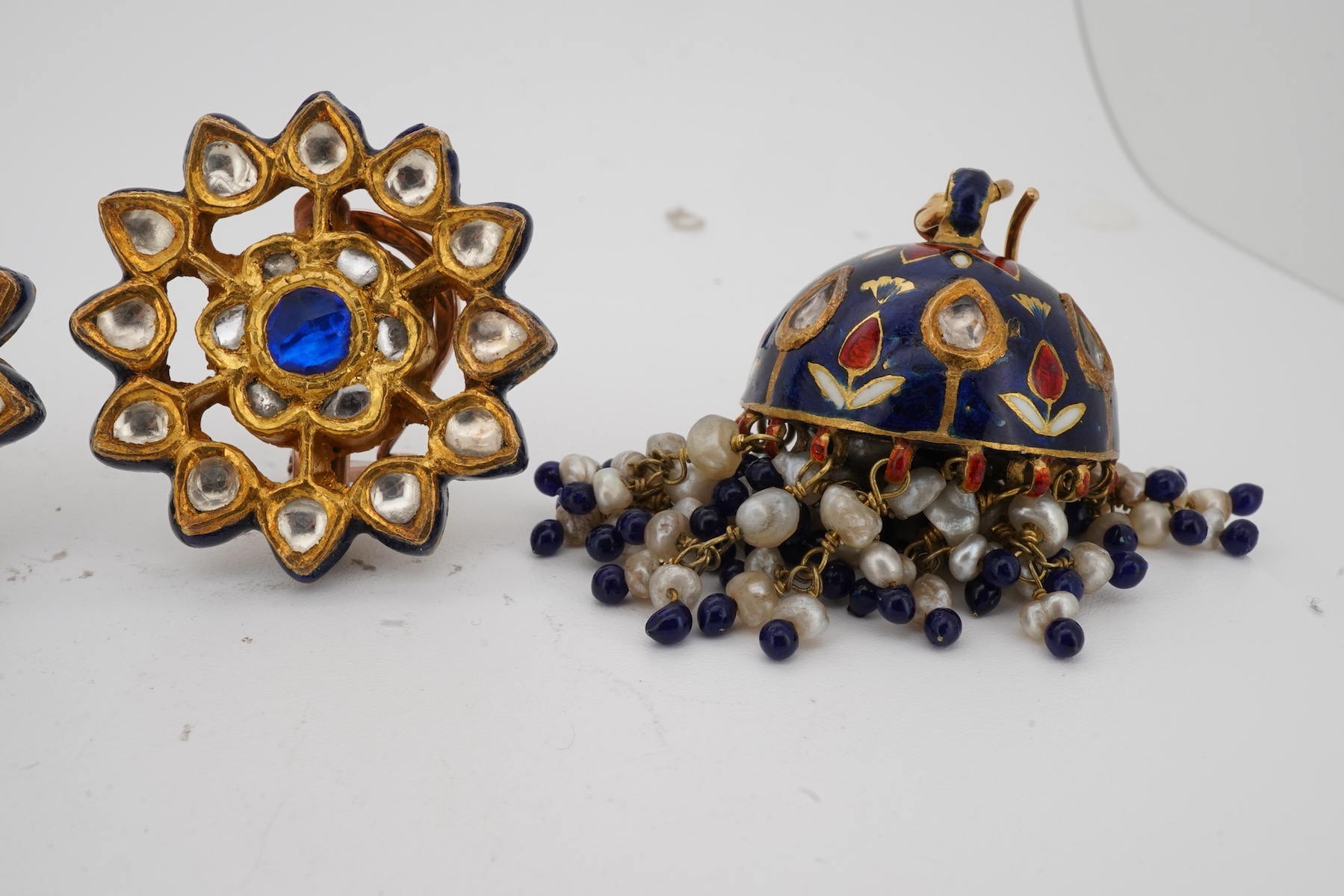 Two pairs of Indian enamelled earrings, comprising: one of chandelier design, set with rock crystals and applied with blue, white and red enamel, suspending a fringe of cultured pearls and blue and red pastes, length 5.1